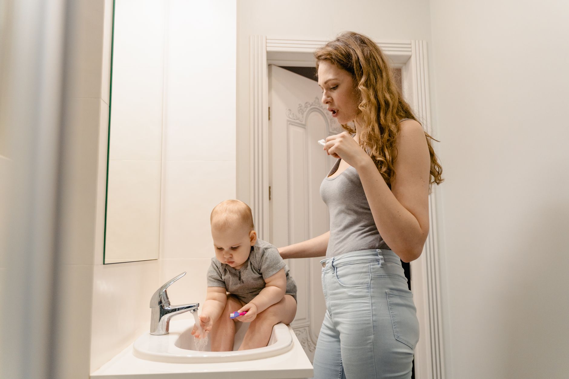 Parent gently brushing a toddler's teeth at the bathroom sink to build healthy dental habits early
